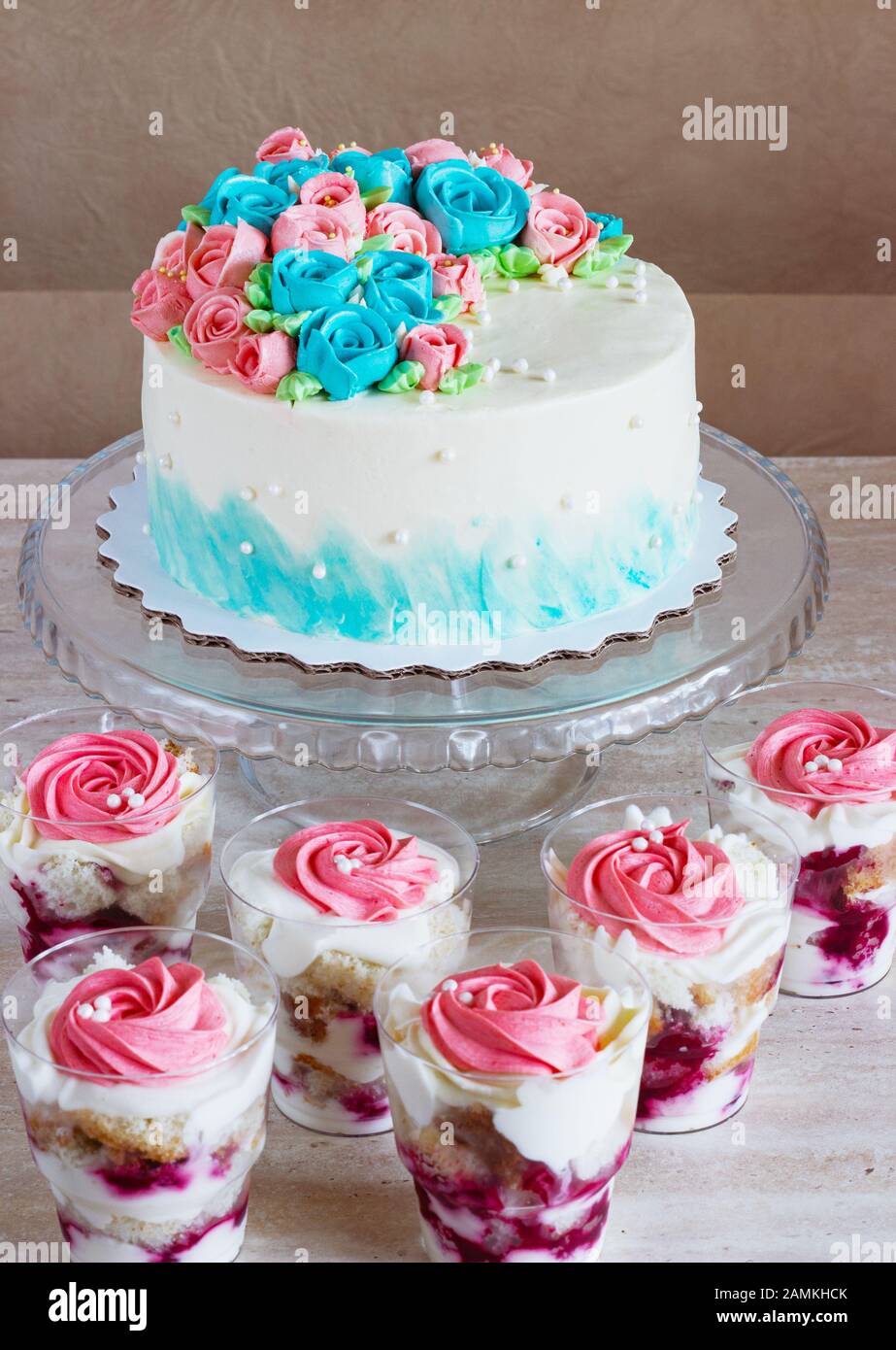 Torta festiva con rose color crema e dessert multistrato con frutta e formaggio cremoso in un vaso di vetro su sfondo chiaro. Foto Stock