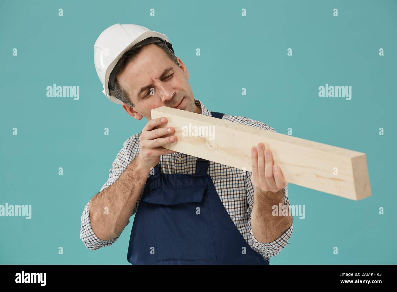 Girovita ritratto di lavoratore professionale che tiene il legno mentre ispeziona la qualità di produzione in piedi contro sfondo blu, copia spazio Foto Stock