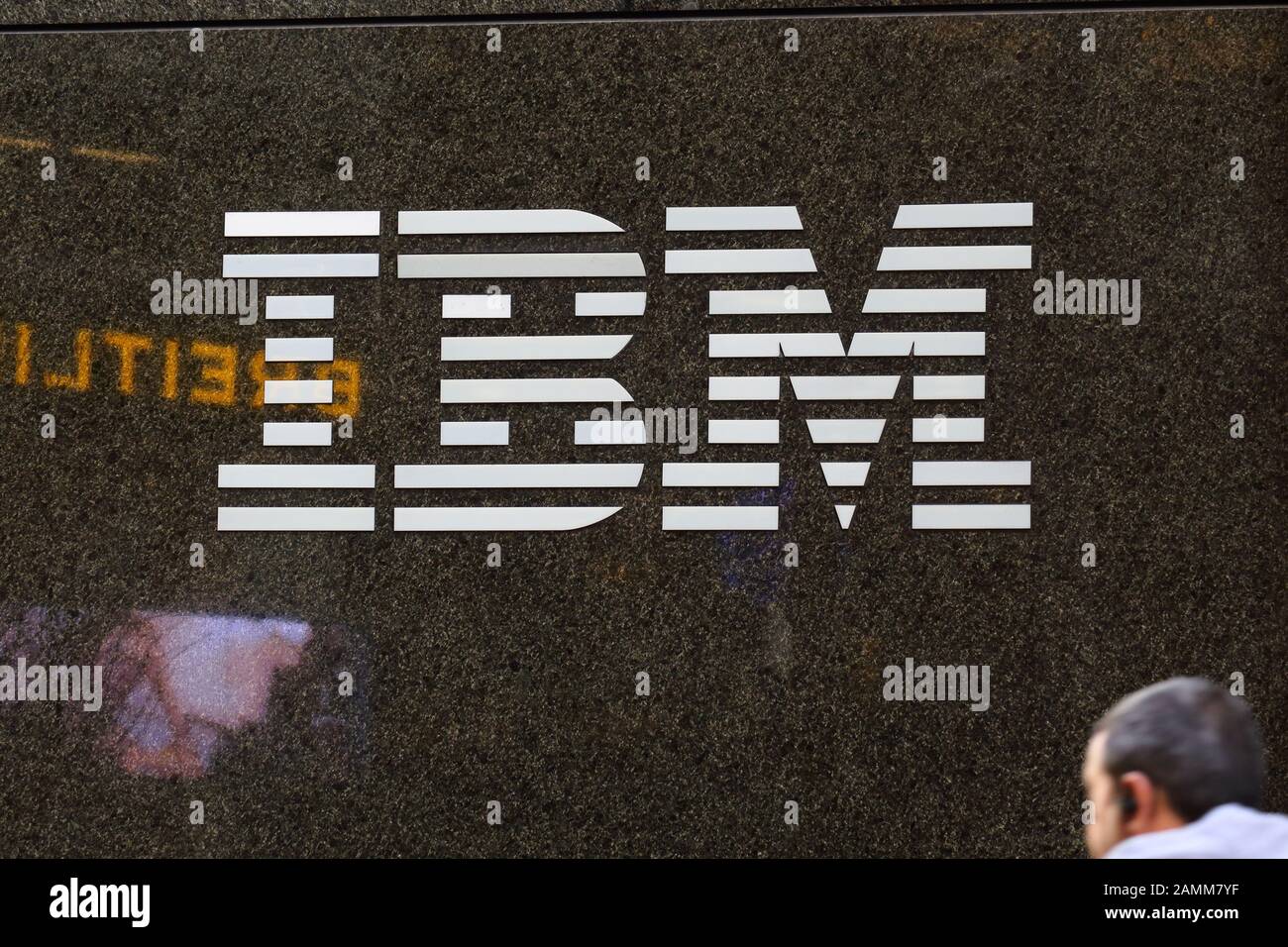 Una persona cammina con un logo IBM su una parete di granito nero a New York, NY Foto Stock