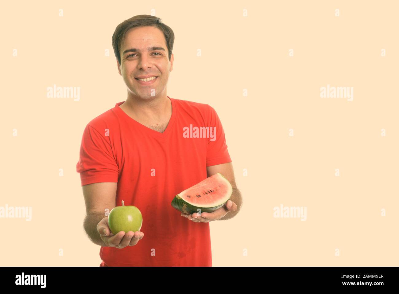 Studio scatto di giovane felice persiano uomo sorridente mentre tenendo fetta di anguria e mela verde Foto Stock