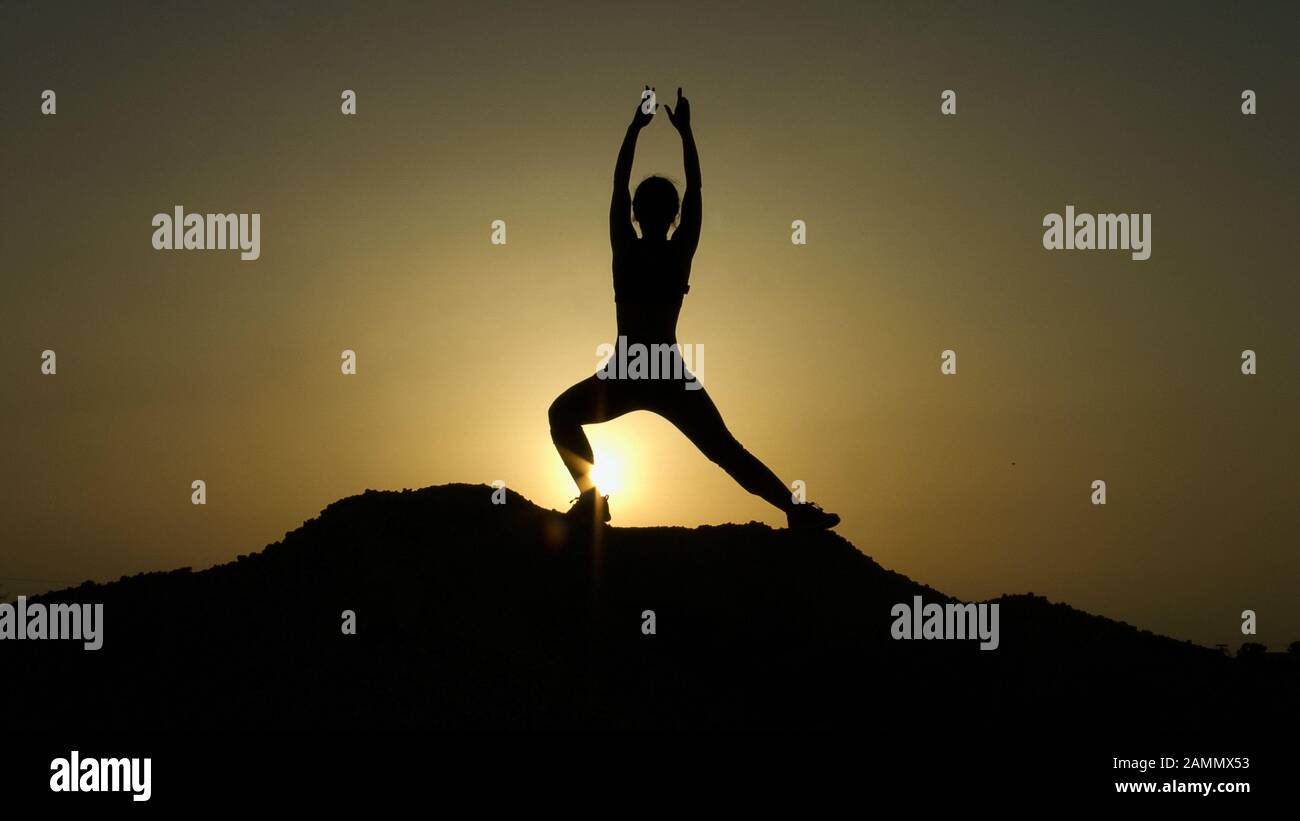 Silhouette di giovane donna che gode armonia con la natura mentre pratica lo yoga Foto Stock