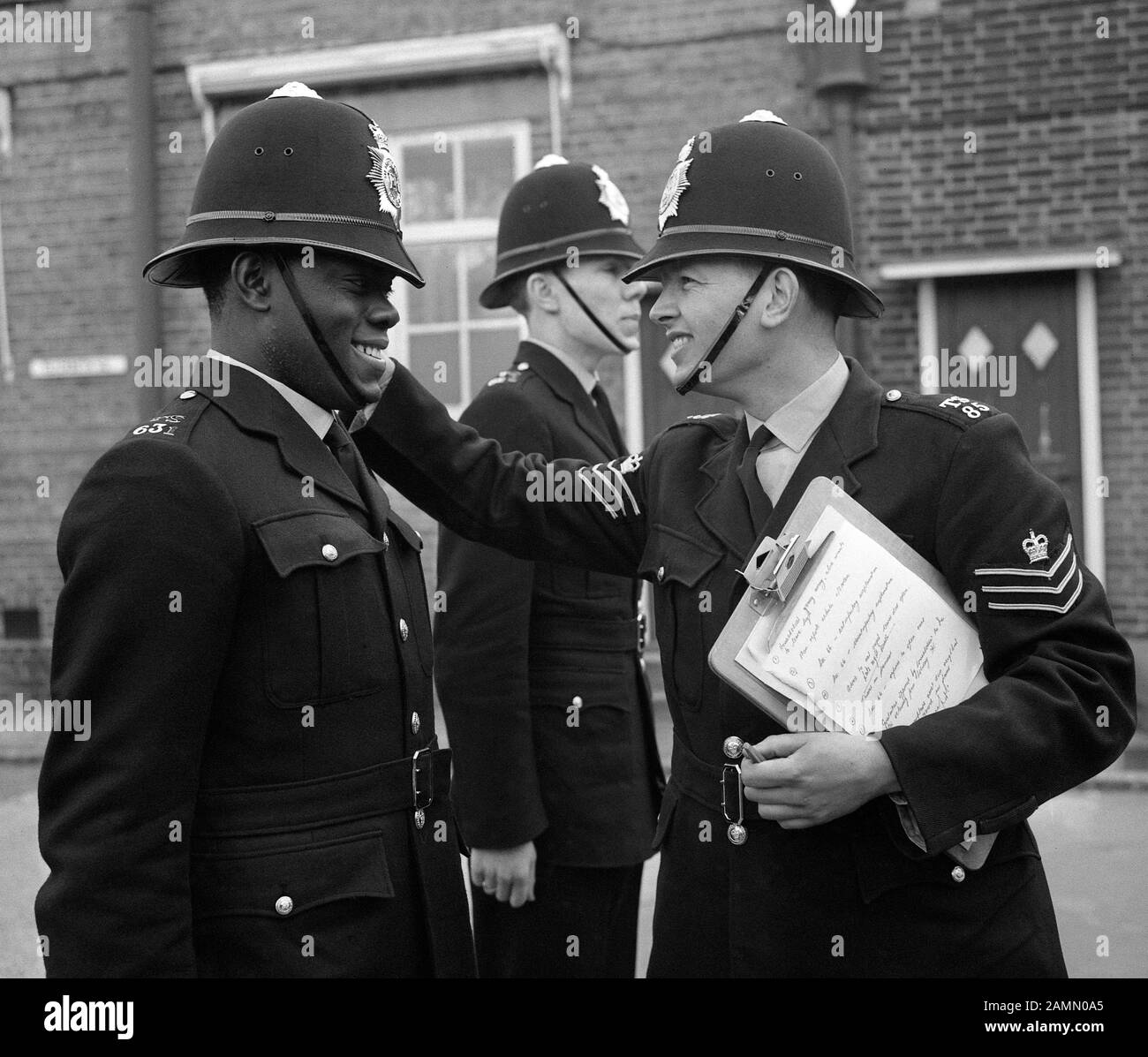 Sotto nove giorni di formazione come il primo poliziotto nero di Londra, PC Norwell Gumbs, 21, al Metropolitan Police Training College di Hendon, Londra, come la stazione Sgt John Aldridge gli indica nel modo corretto di indossare il suo casco. Foto Stock