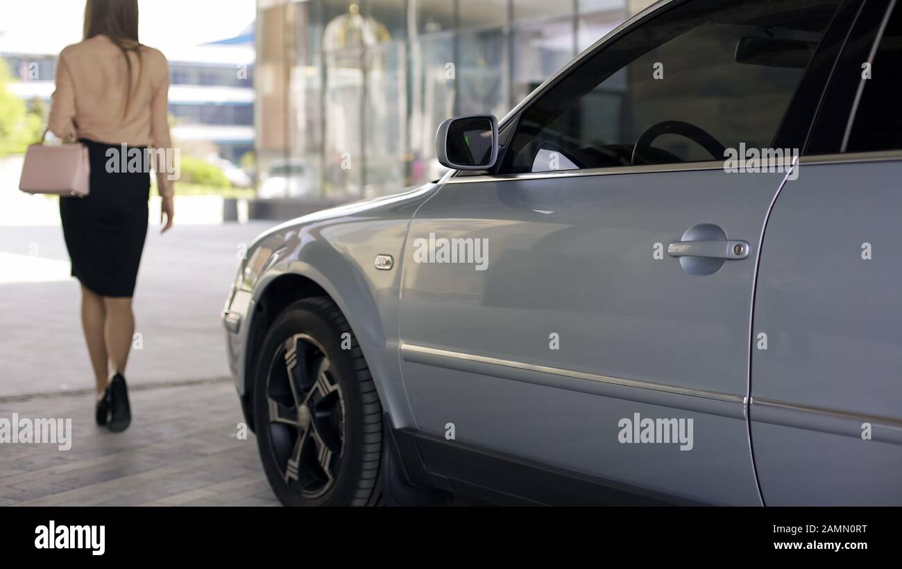 Elegante donna sottile a piedi al centro affari, parcheggio auto nelle vicinanze, vista sul retro Foto Stock