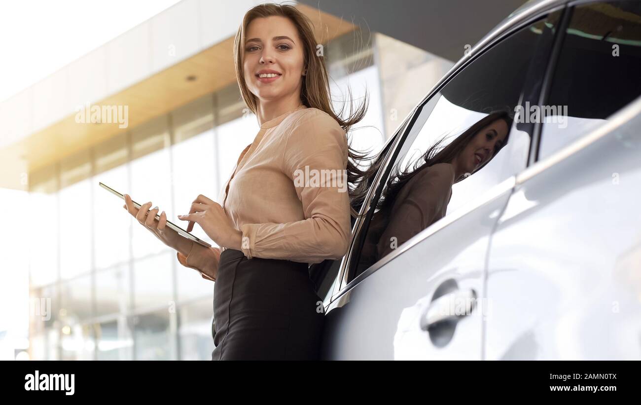Graziosa donna di affari che tiene il tablet, in piedi vicino all'automobile, che posa per la macchina fotografica Foto Stock