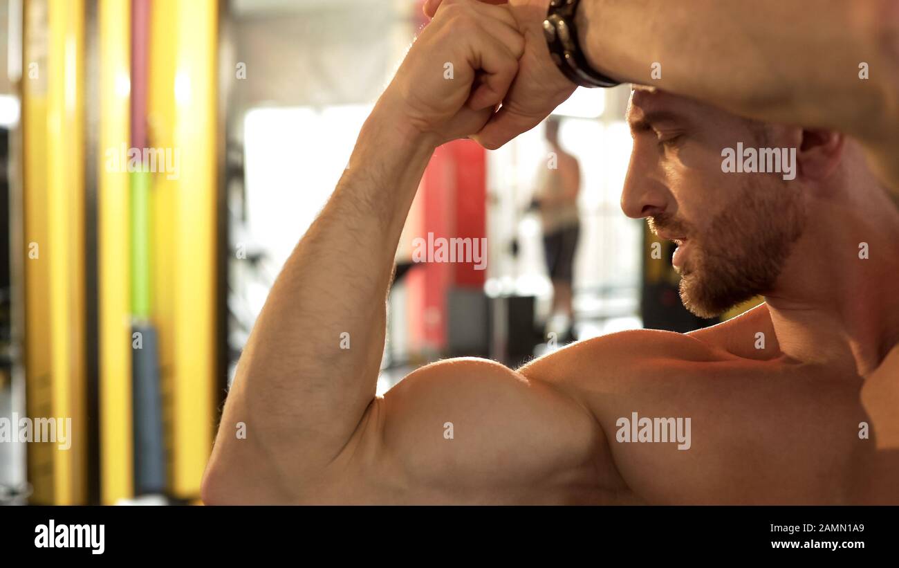 Fit maschio ammirando i suoi muscoli sviluppati, facendo bicep posa palestra, orgoglioso di risultato Foto Stock