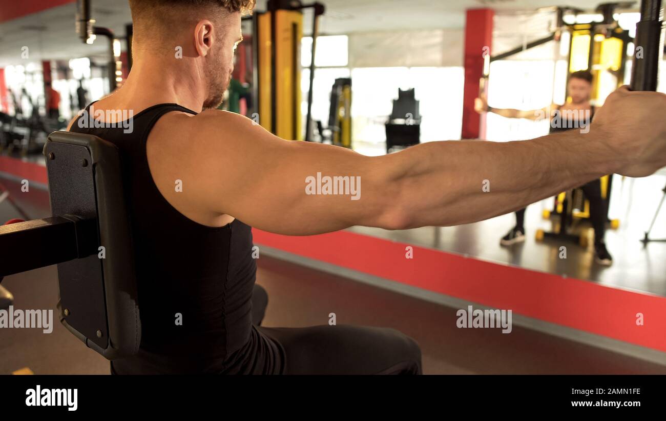 Uomo che pompa i suoi muscoli pettorali in palestra, guardando la sua riflessione in specchio Foto Stock