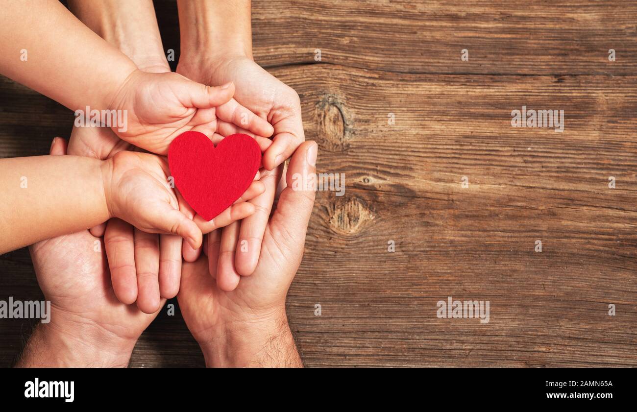 mani di famiglia che tengono il cuore rosso su sfondo di legno. Donazione, beneficenza, concetto di salute Foto Stock