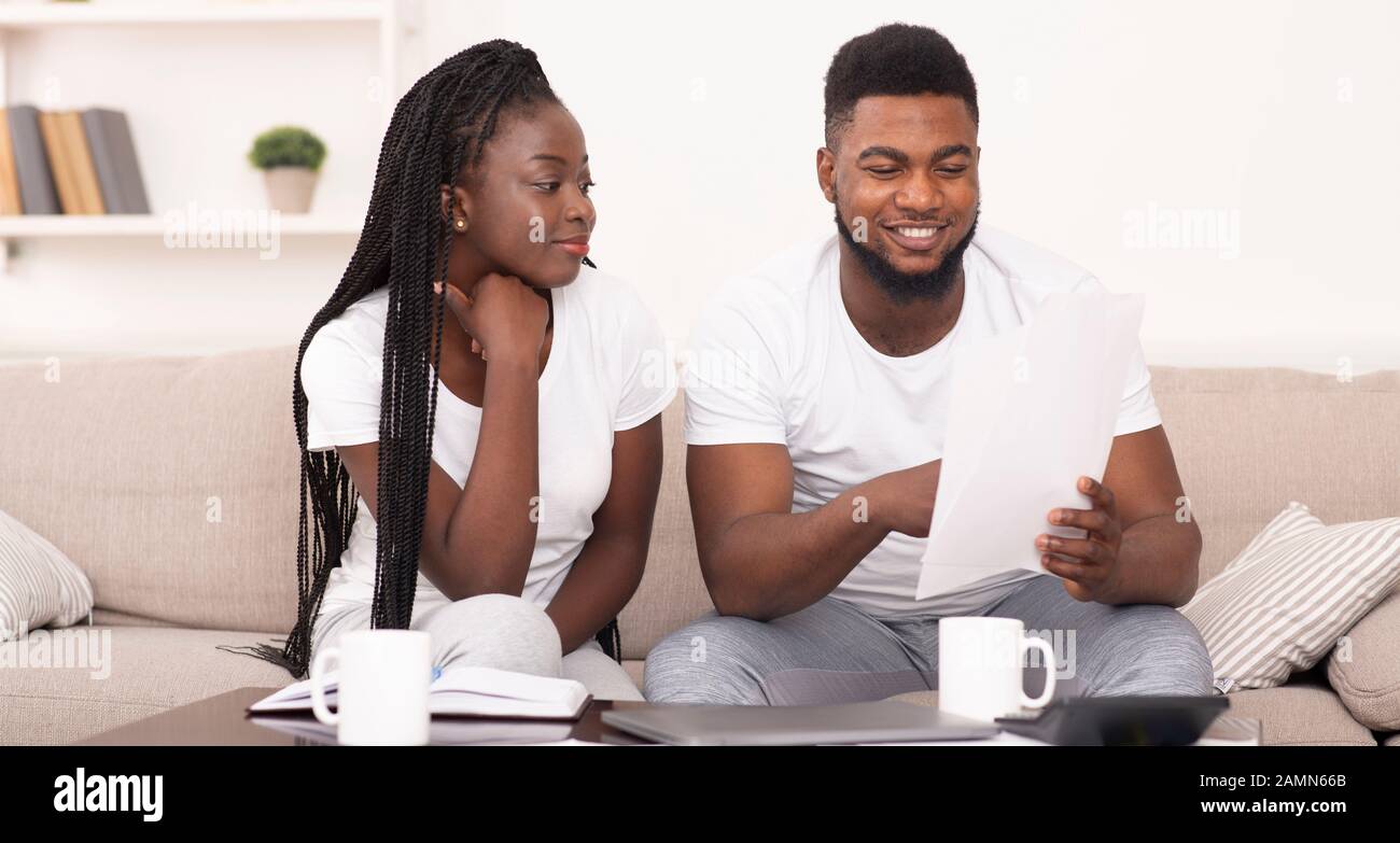 Sorridente coppia nera che legge le carte di assicurazione a casa, controllando i dettagli dell'accordo Foto Stock