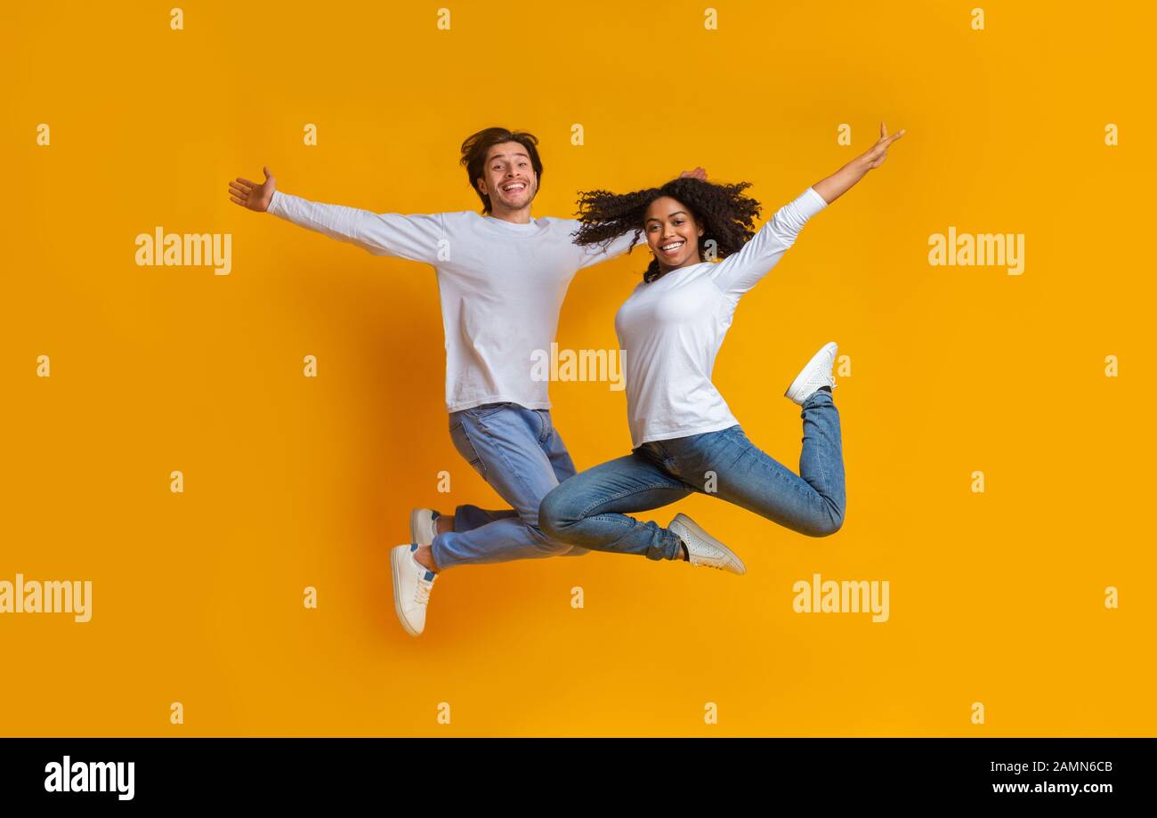 Spensierata coppia interracial saltando in aria con le braccia spalmate Foto Stock