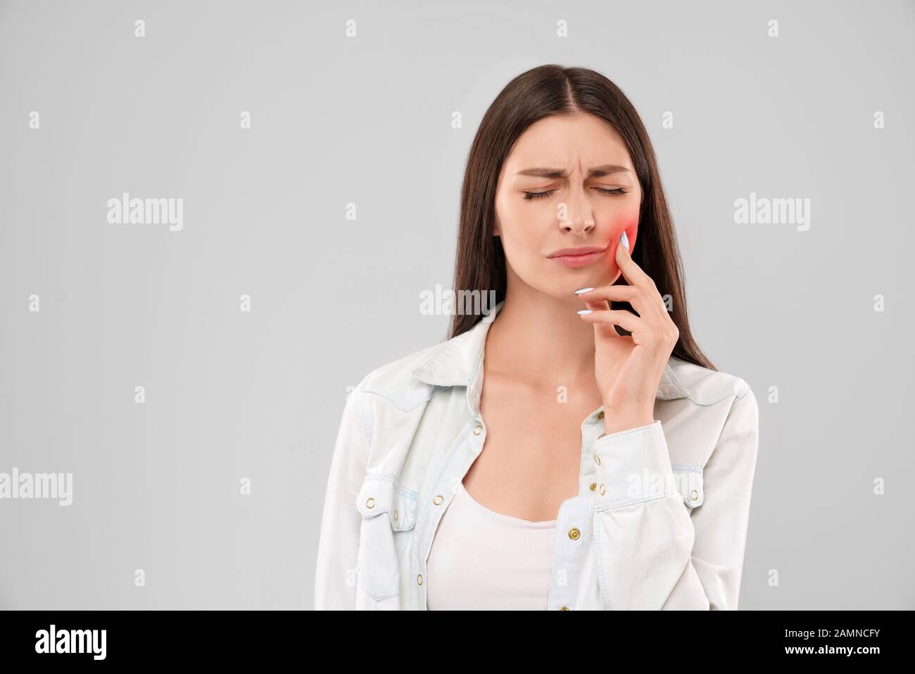 Giovane donna caucasica in maglia bianca su grigio Sfondo isolato di toccare la bocca con la mano con espressione dolorosa a causa di mal di denti. Vista frontale della bruna con gli occhi chiusi. Concetto di dentista. Foto Stock