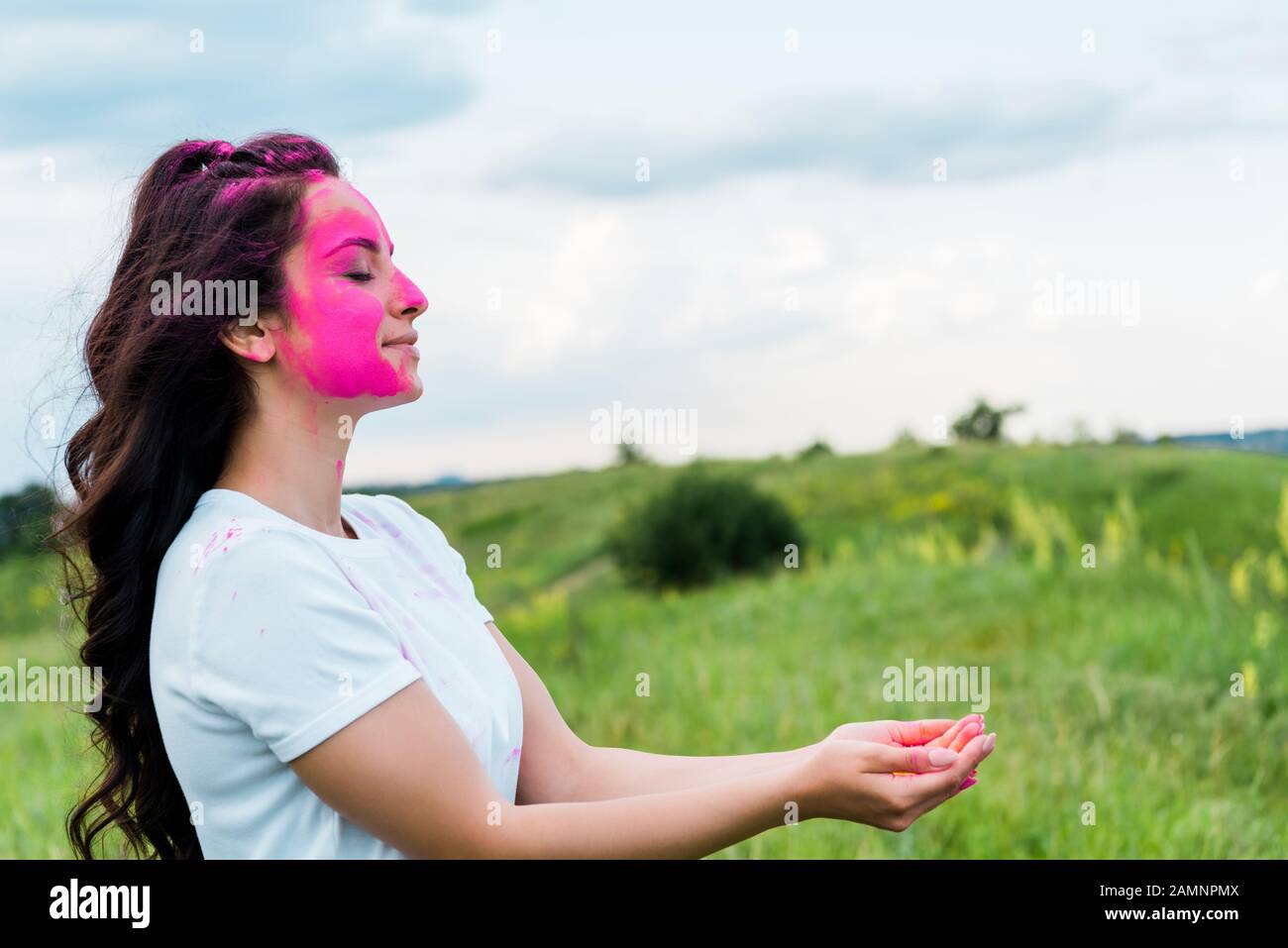 donna felice con vernice holi rosa sul viso in piedi con le mani cucciate Foto Stock