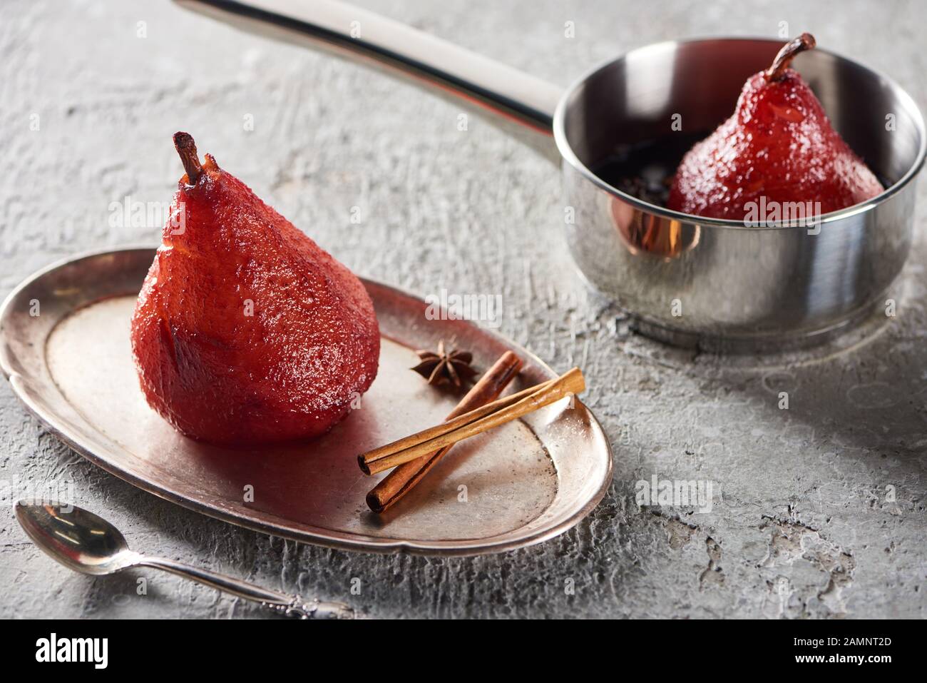 deliziosa pera al vino in padella e su piatto d'argento con cannella e anice su superficie di cemento grigio Foto Stock