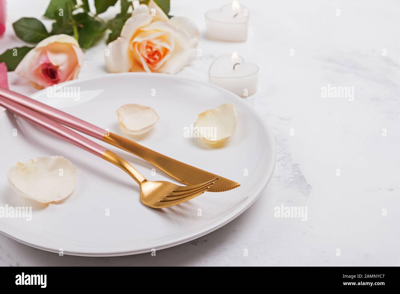 Piastra con la forchetta e il coltello e petali di rosa e rose un tavolo bianco di close-up. Foto Stock