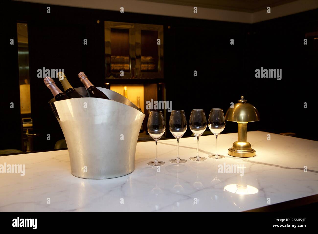 La benna di champagne e bicchieri su un bancone di marmo in una illuminata vivamente il bar dell'hotel. Foto Stock