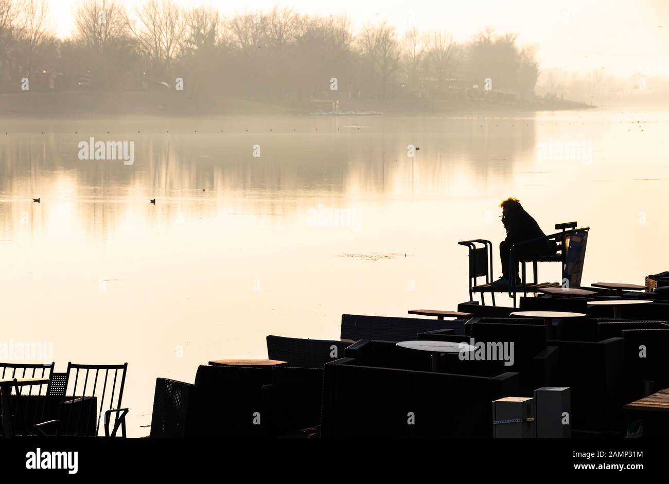 Silhouette di una persona seduta da sola sulla riva del fiume e fumare mentre si guarda l'altra riva Foto Stock