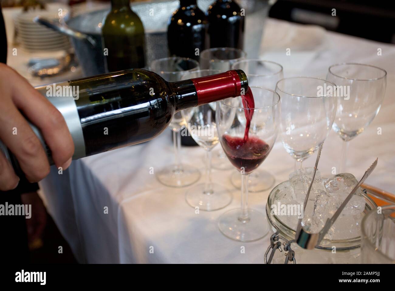 Primo piano di un cameriere che versa un bicchiere di vino rosso in un evento sociale. Foto Stock