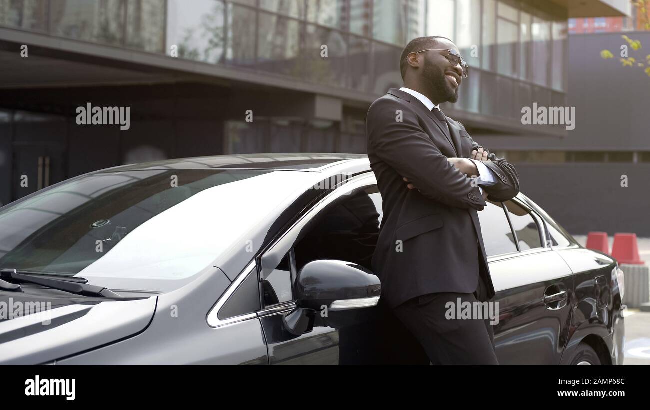Bell'uomo afroamericano sorridente sinceramente stare vicino alla sua auto, buone notizie Foto Stock