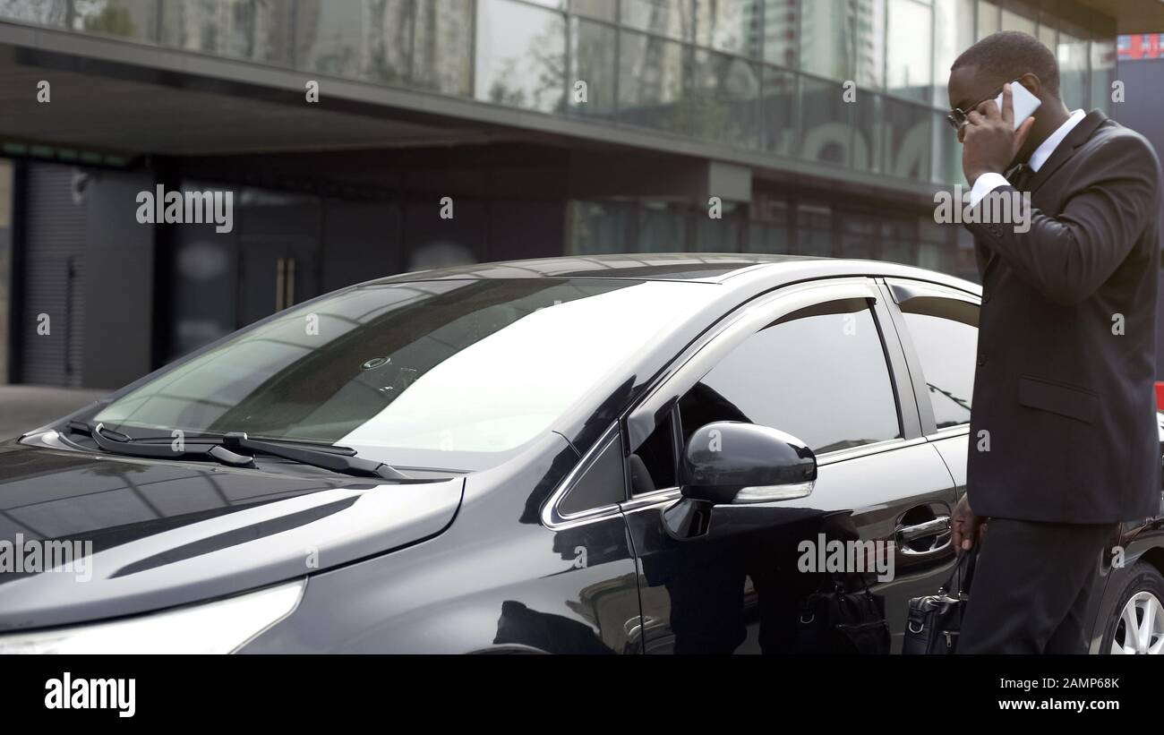 Uomo afro-americano che viene alla sua auto sul parcheggio che parla su mobilephone Foto Stock