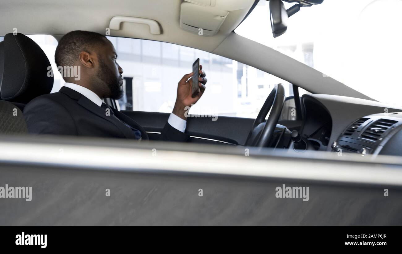 Driver in attesa di boss, noioso scorrimento news applicazione sul suo smartphone Foto Stock