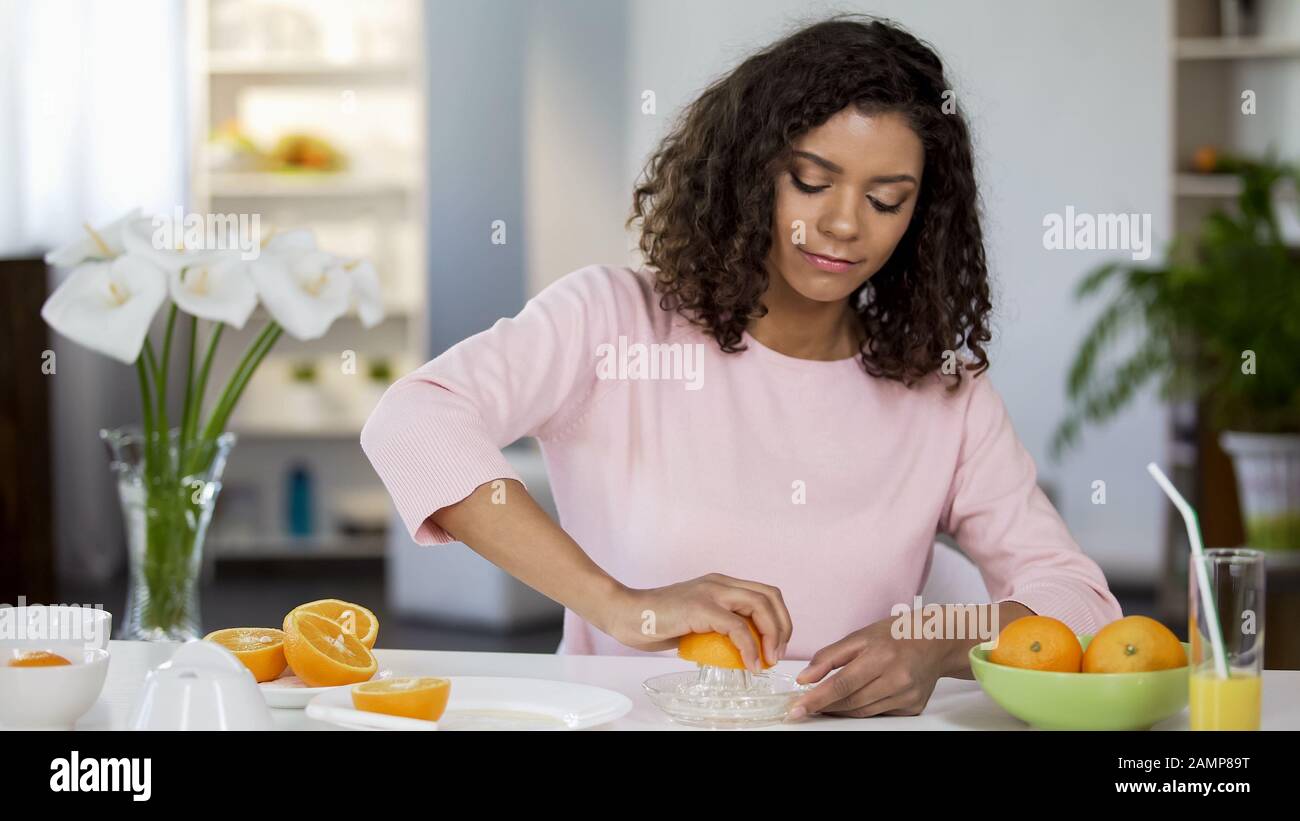 Giovane donna di razza mista che spremono succo d'arancia, peso e controllo della salute, dieta Foto Stock