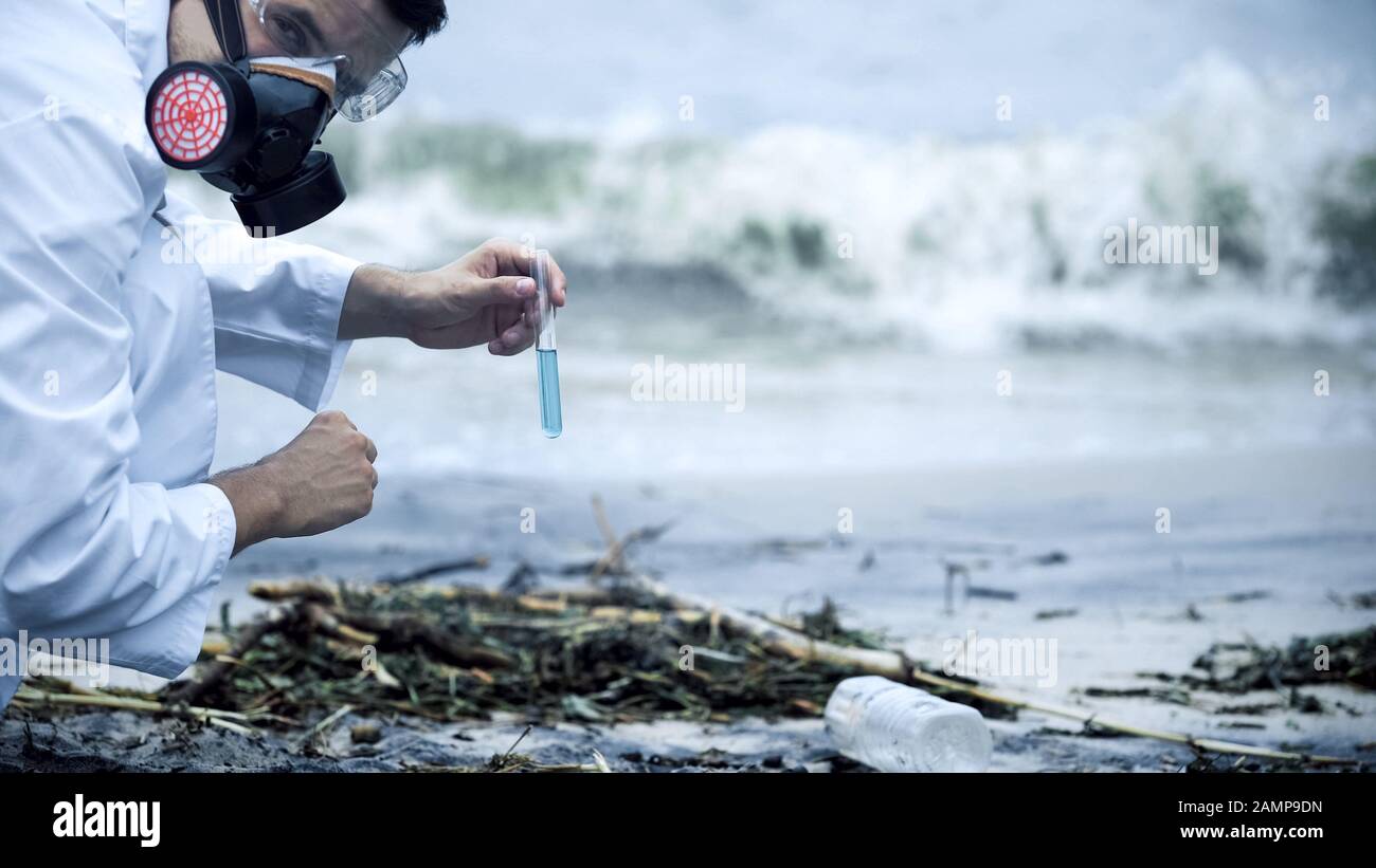 Tossicologo che controlla l'acqua inquinata, spruzzi sulla riva, disastro ambientale Foto Stock