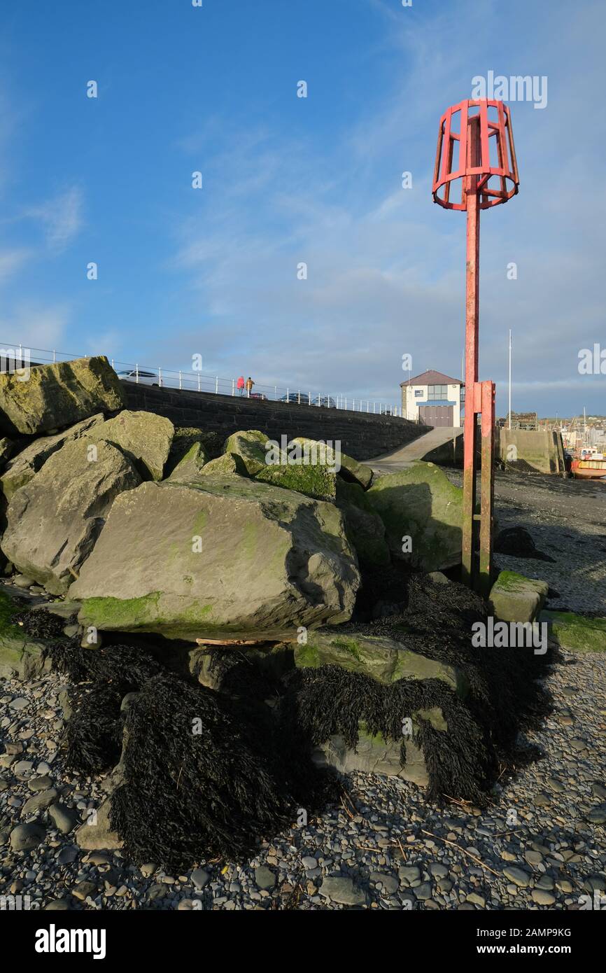 Porto di Aberystwyth: Rosso alto maree marcatore contro cielo blu sfondo e grandi massi Foto Stock