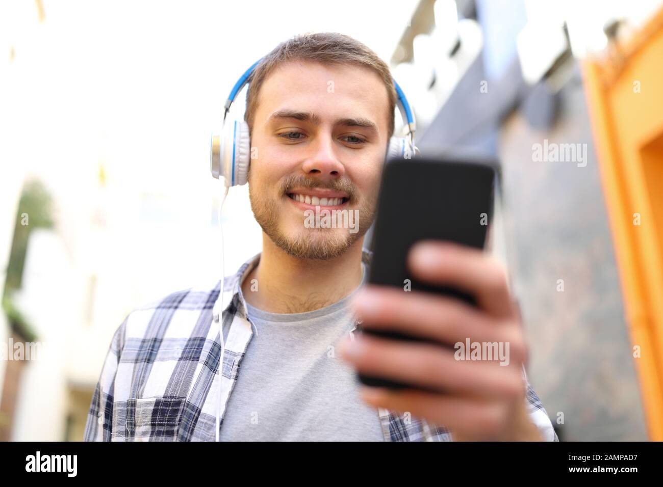 Vista frontale dell'uomo felice che ascolta la musica controllando lo smartphone camminando in strada Foto Stock