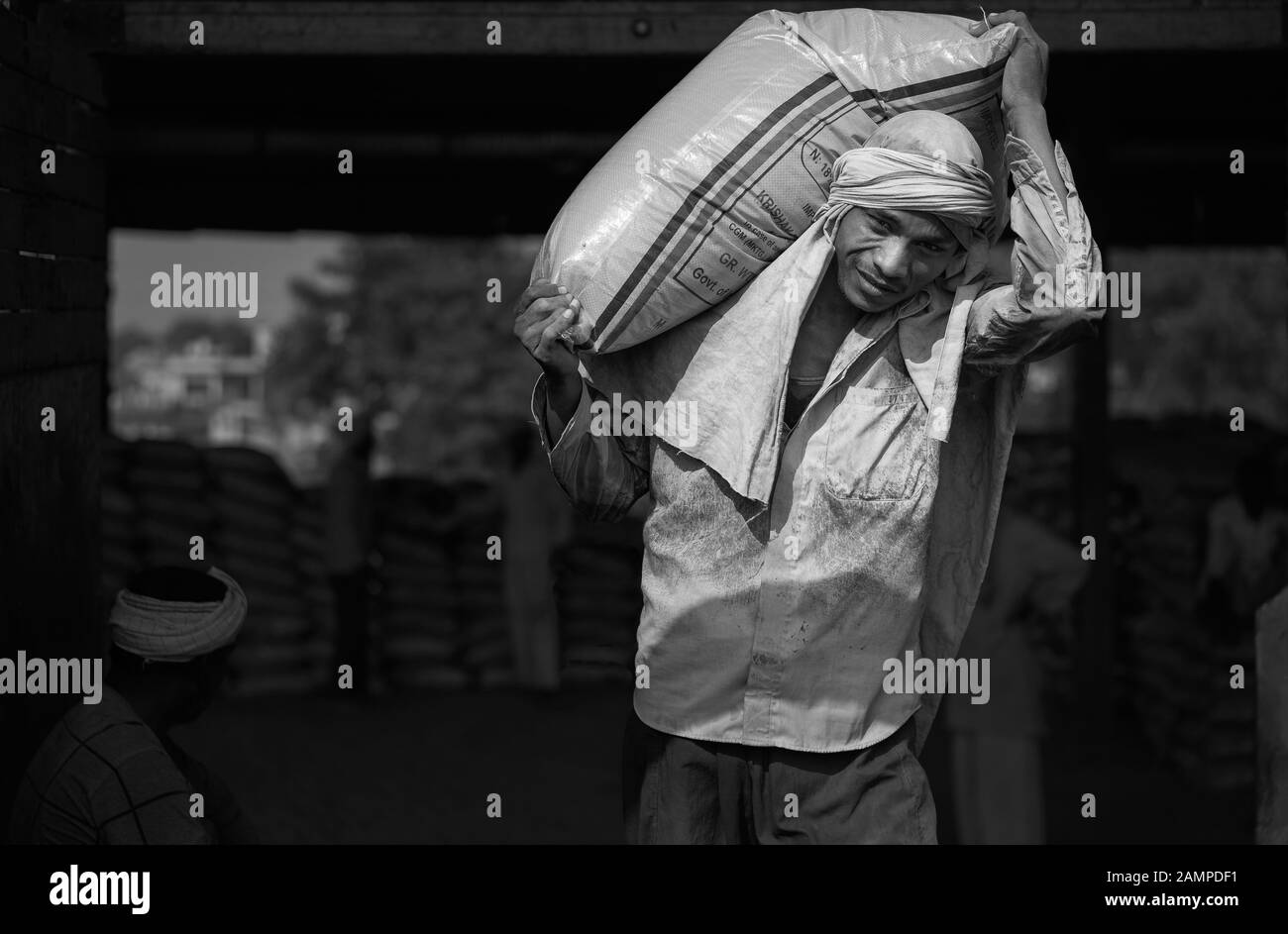 L'uomo lavora per scaricare la borsa di cemento in condizioni polverose dal treno in caldo estate in Mathura, Uttar Pradesh, India. Foto Stock