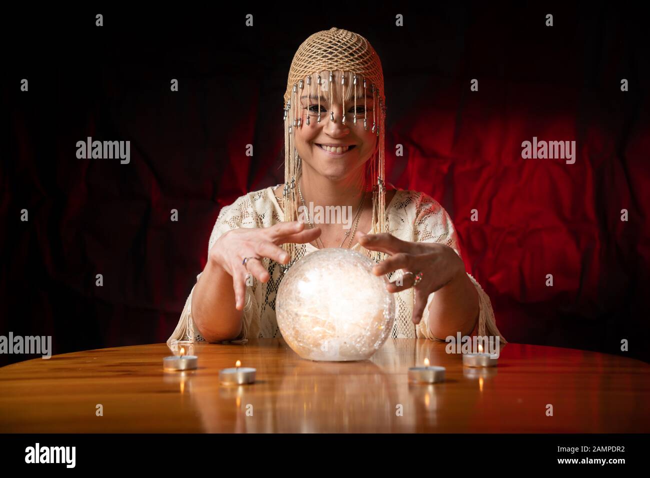 Fortune Teller con Crystal Ball sul tavolo con candele e sfondo nero e rosso chiazzato Foto Stock