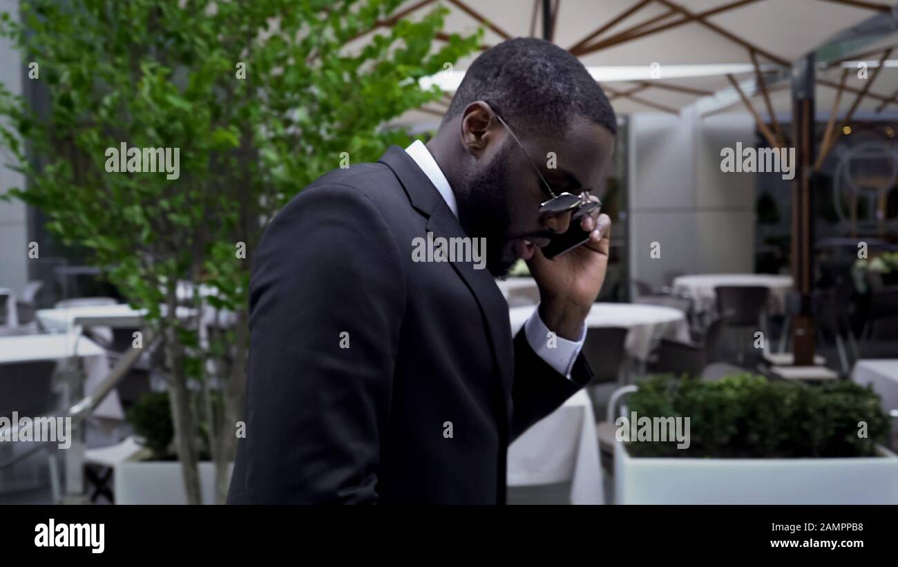 Uomini in business suit passando da un lussuoso caffè all'aperto che parla sul telefono cellulare Foto Stock