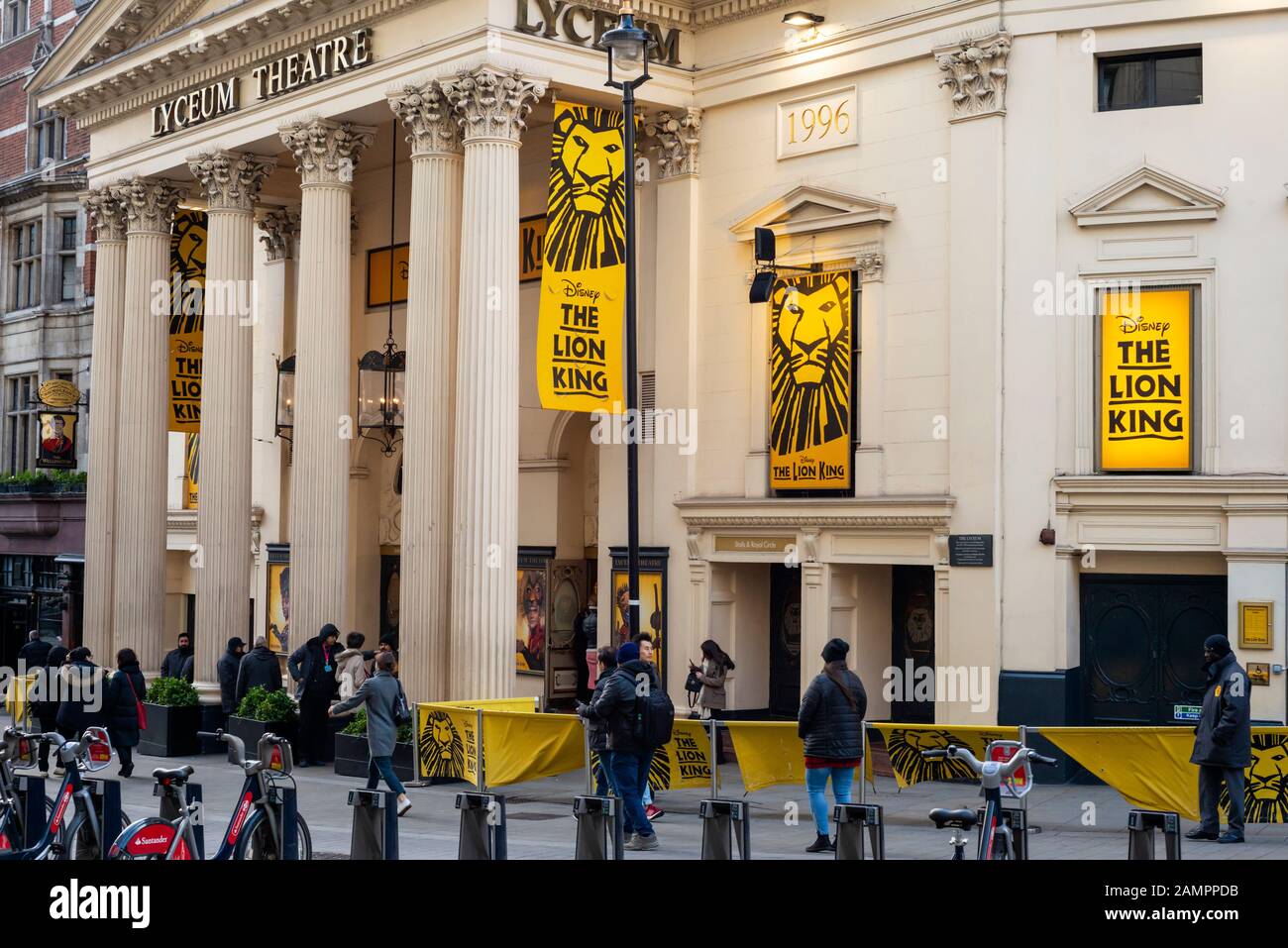 Persone che camminano oltre il Lyceum Theatre di Londra coperto di giallo poster che presenta lo spettacolo musicale Lion King a Covent Garden Londra come gennaio 2020 Foto Stock