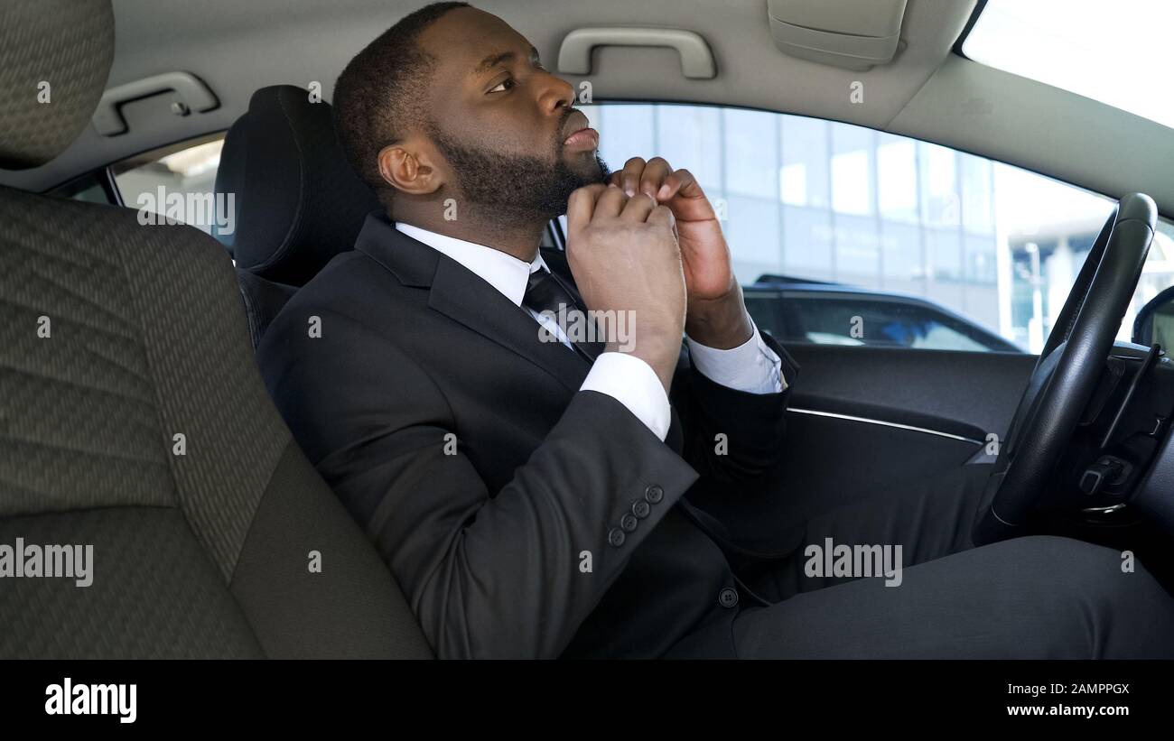 Uomo d'affari afro-americano che si sta muovendo per la barba, guardando lo specchio per auto posteriore Foto Stock