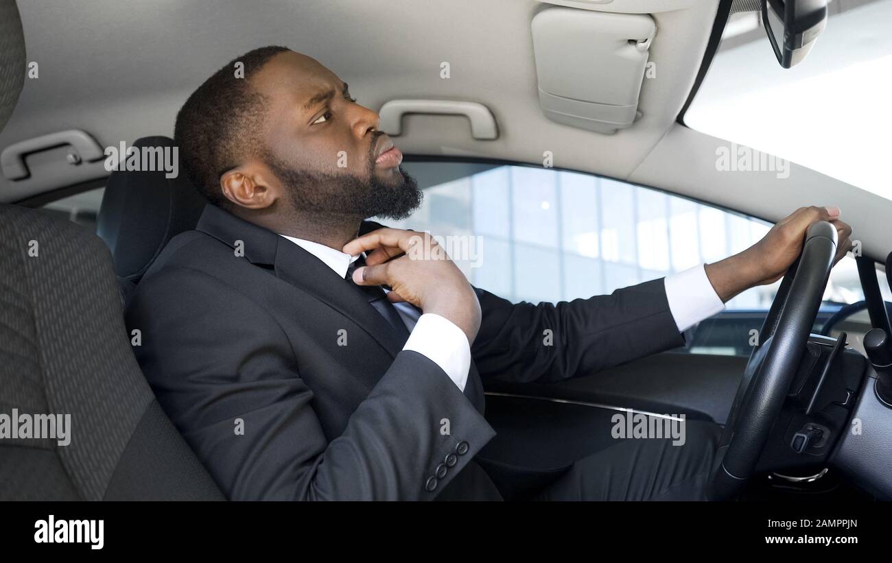 Uomo d'affari sicuro di sé seduto in auto, guardando in specchio per intelligente cravatta Foto Stock