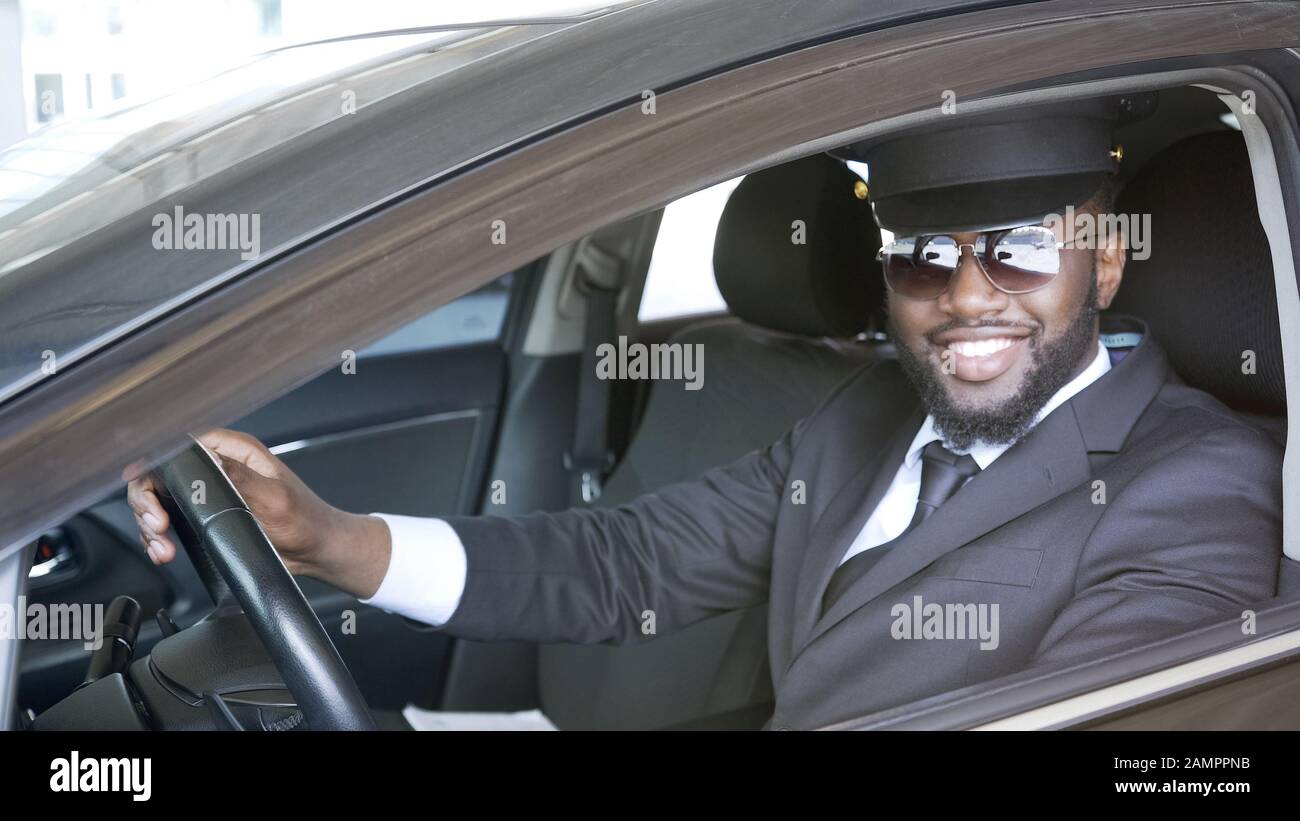 Autista maschio nero seduto in auto e sorridente in macchina, servizio di trasporto Foto Stock