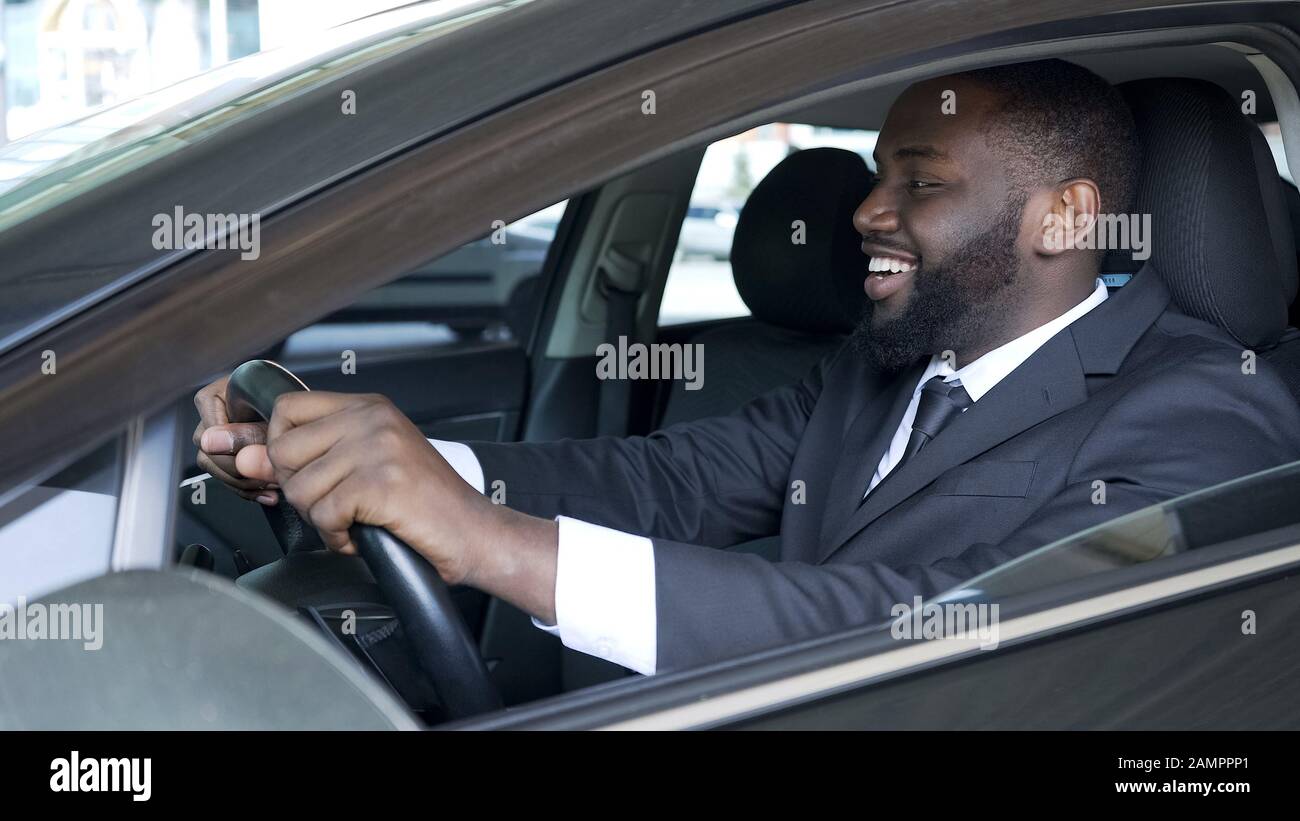 Uomo americano africano seduto in macchina costosa soddisfatto e sorridente, prova su strada Foto Stock