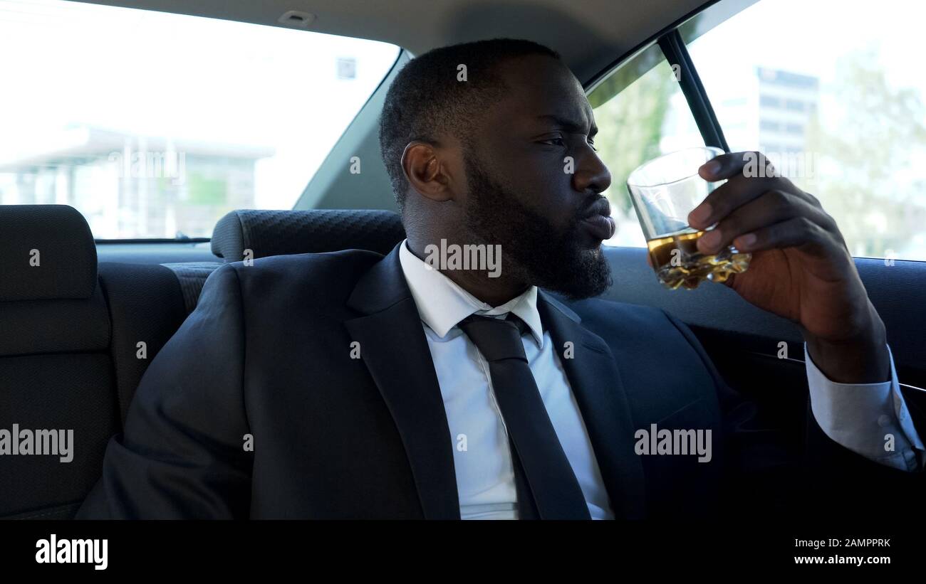 Uomo ricco sicuro di sé che beve alcol in auto, stile di vita di lusso, successo Foto Stock