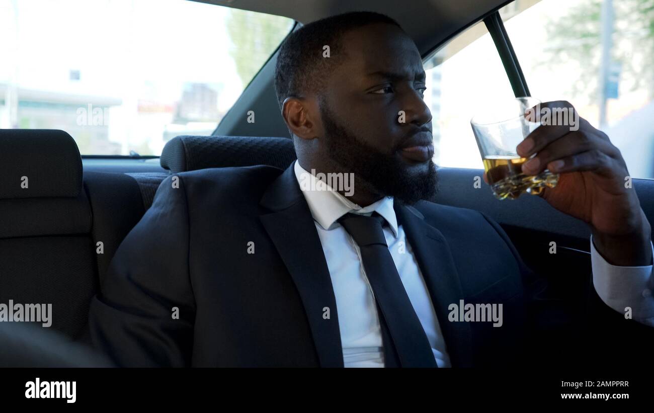 Uomo africano americano pensieroso seduto sul sedile posteriore dell'automobile con bevanda alcolica Foto Stock