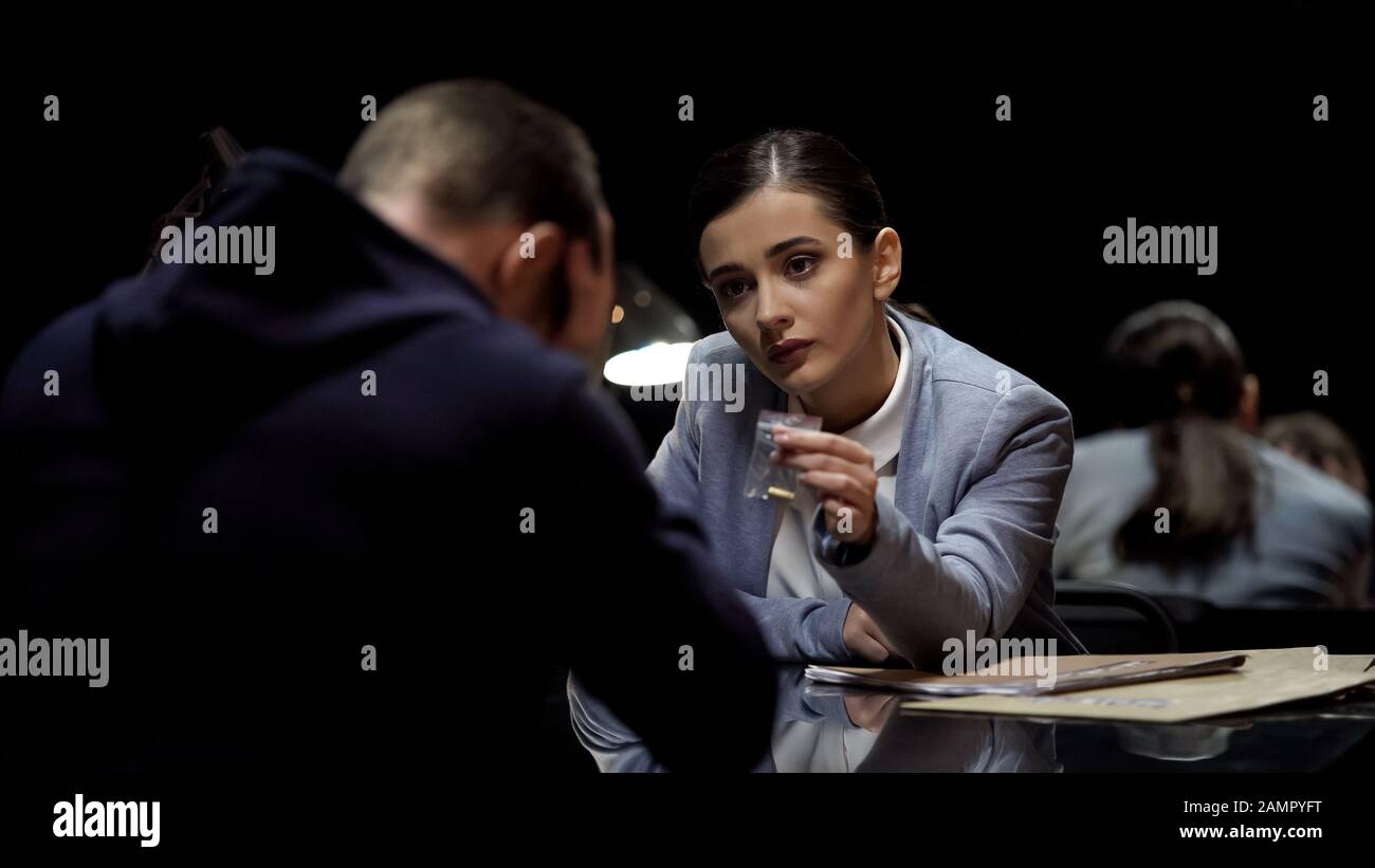 Agente di polizia femminile che mostra prove fisiche pallottole, guardando la reazione sospetta Foto Stock