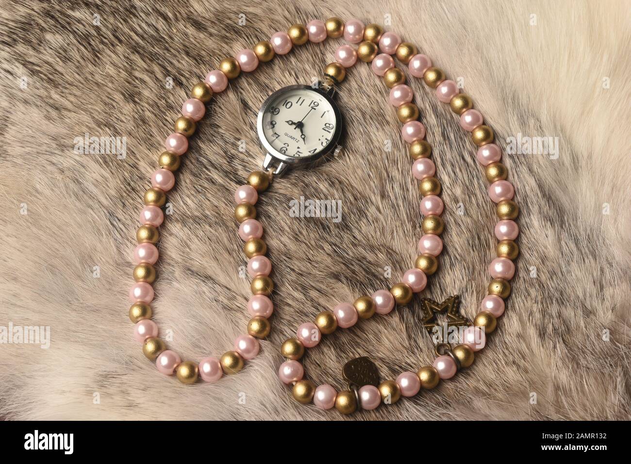 Orologio da polso con collana di perle su pavimento in pelliccia sintetica Foto Stock