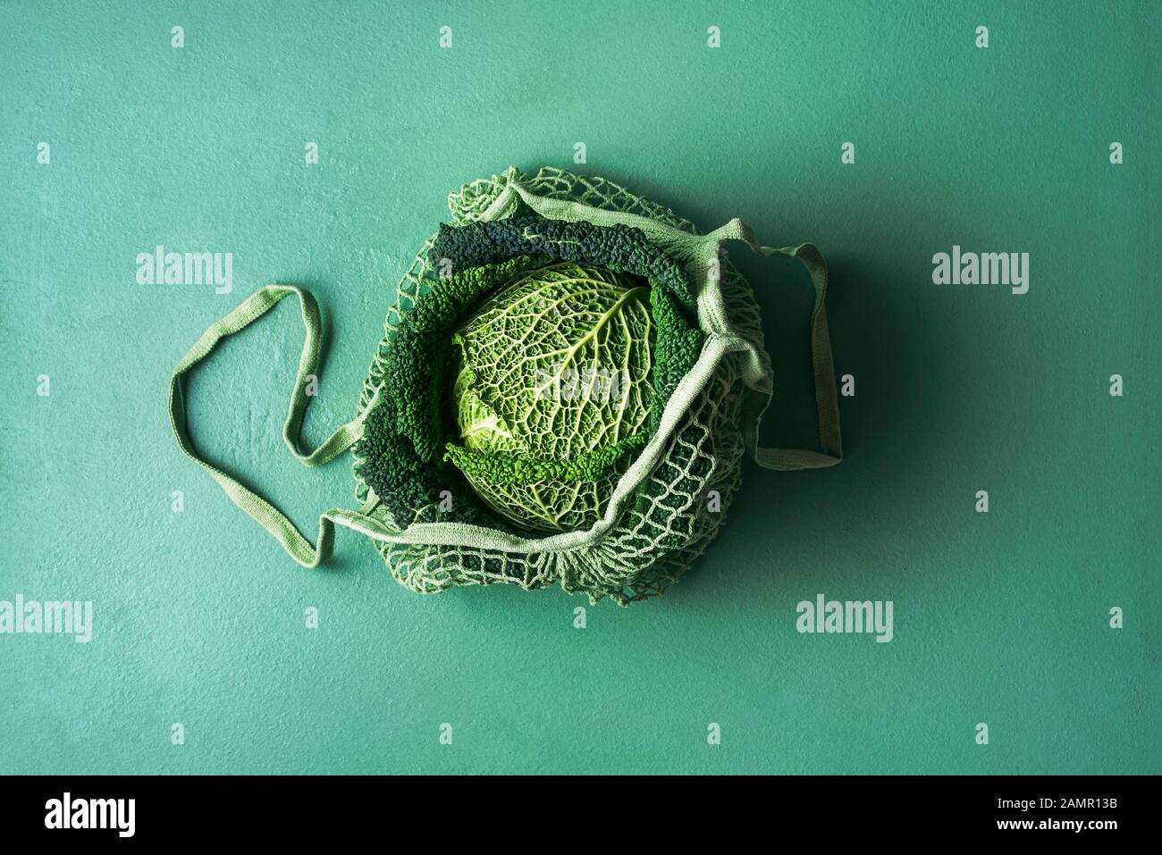 Cavolo biologico verza in una borsa riutilizzabile in acqua menthe tavolo. Sacchetto di rete in tessuto con cavolo fresco. Immagine monotona verde con un singolo cavolo. Foto Stock