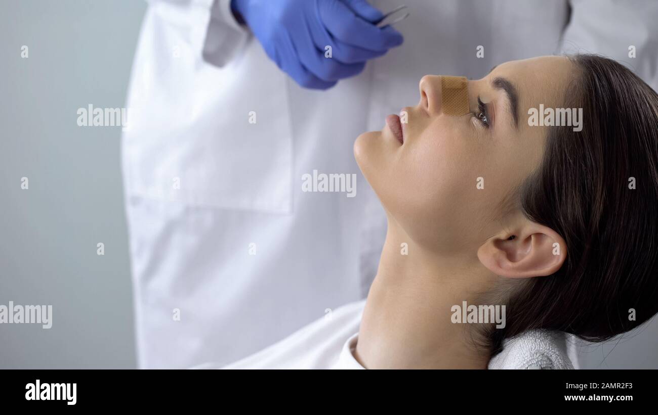 Signora con intonaco sul naso, medico che esamina il viso dei pazienti dopo chirurgia plastica Foto Stock