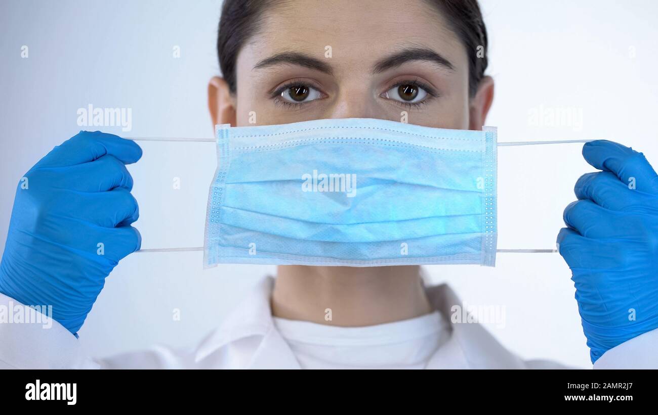 Giovane signora medico che mette sulla maschera chirurgica, la sicurezza durante l'esame, closeup Foto Stock