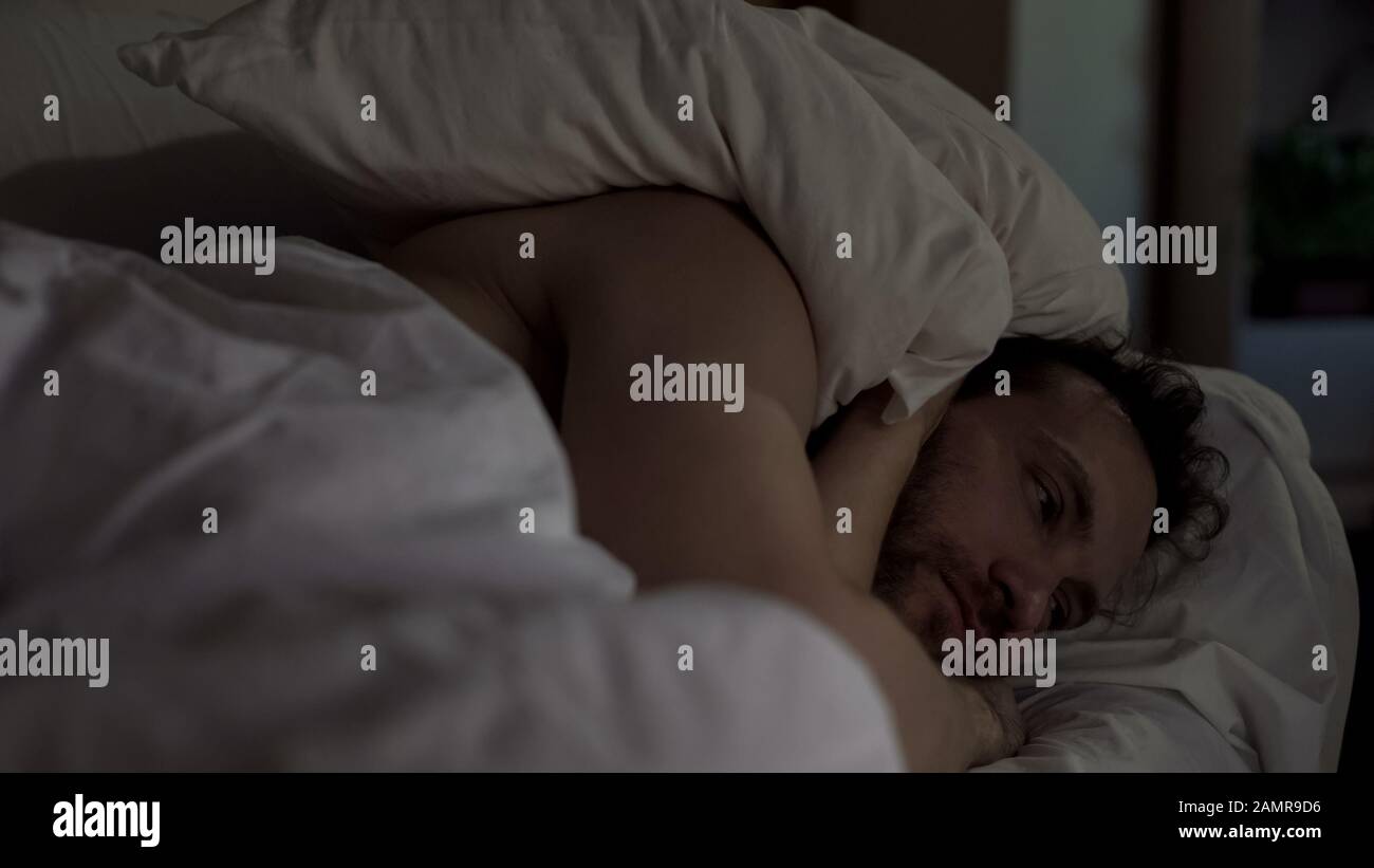 L'uomo infastidito che si lancia e si gira a letto non riesce a addormentarsi, vicini rumorosi Foto Stock