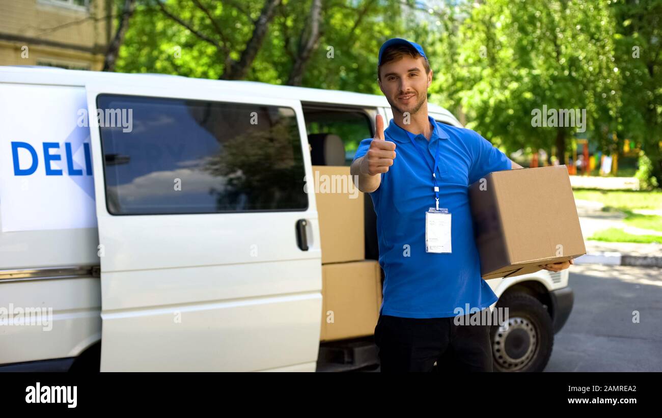 Il lavoratore postale che prende il pacco dal furgone di consegna e mostra pollici in su Foto Stock