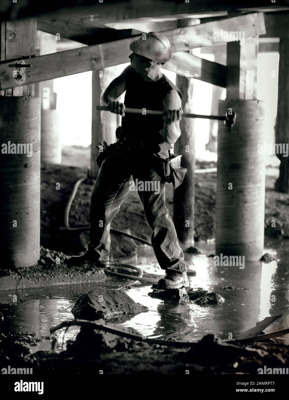 Operaio di costruzione maschio che si prepara a colpire un chiodo con un mazzuolo grande sotto una casa. Foto Stock