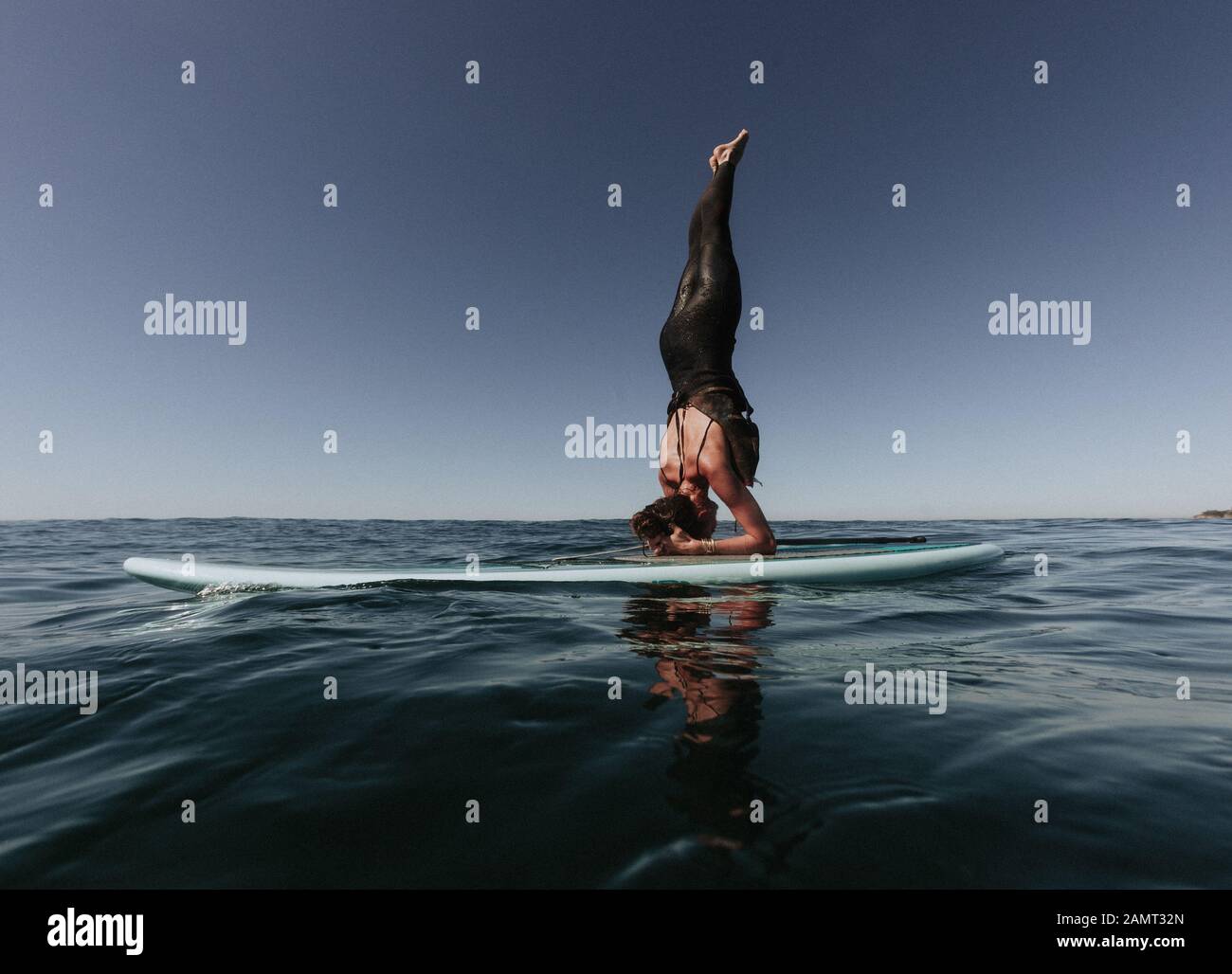 Donna che fa un headstand su un paddleboard, Laguna Beach, California, Stati Uniti Foto Stock