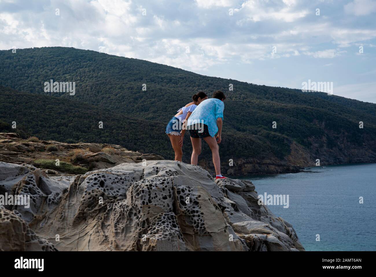 Uomo e donna in piedi su rocce che si affacciano sul mare, Golfo di Baratti, Italia Foto Stock