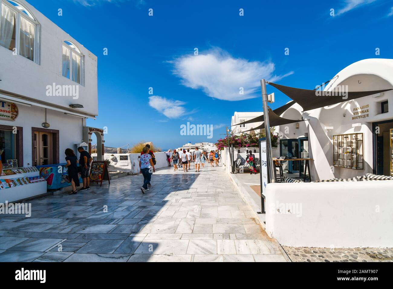I turisti camminano lungo il sentiero superiore passando davanti a negozi e caffetterie in una giornata estiva a Oia sull'isola di Santorini, in Grecia. Foto Stock