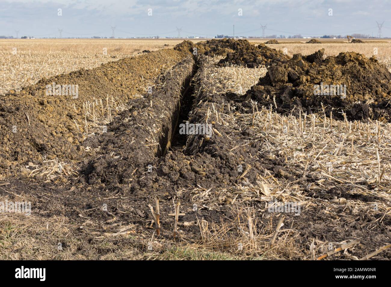 Trincea scavata nel campo di fattoria con cumuli di terra. L'acqua della tubazione di drenaggio, campo di installazione di piastrelle Foto Stock