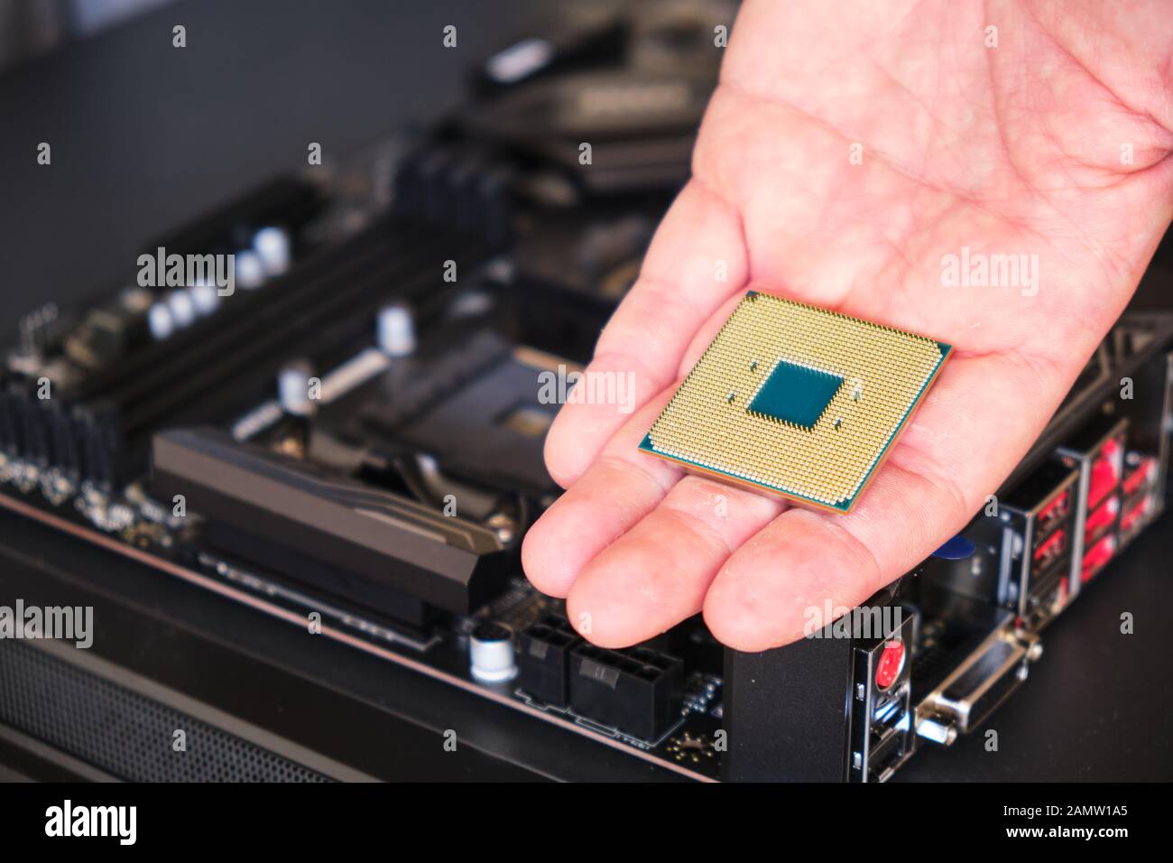 CPU (Central Processing Unit) tenuto in mano - primo piano, con una scheda madre sfocata in background. Spazio di copia. Foto Stock